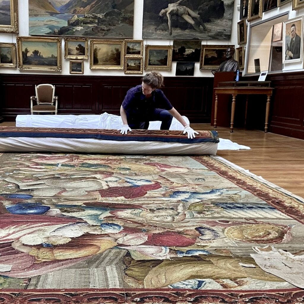 Femme qui enroule une tapisserie pour la conserver selon des méthodes adaptées.
